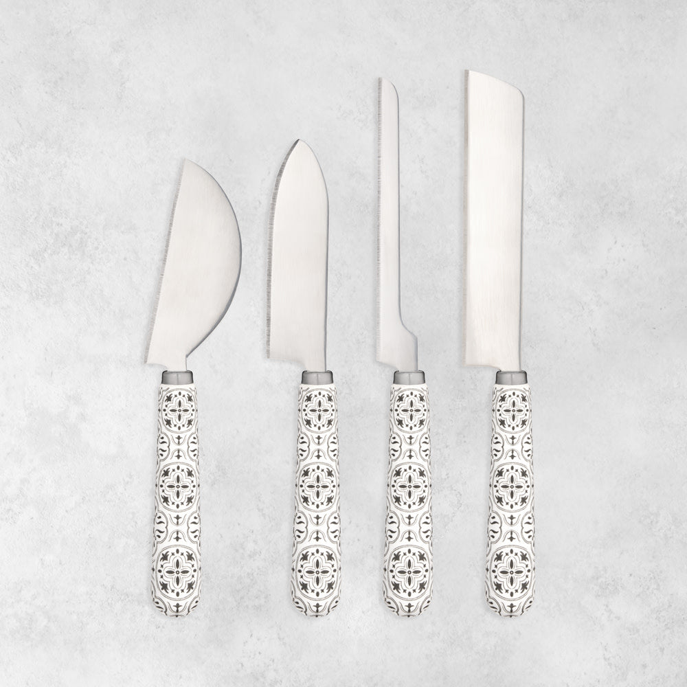 Four cheese knives with different blade shapes and matching tile-patterned ceramic handles on a gray background.