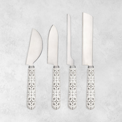 Four cheese knives with different blade shapes and matching tile-patterned ceramic handles on a gray background.