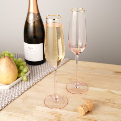 Two champagne flutes with a bottle of champagne on a wooden table.
