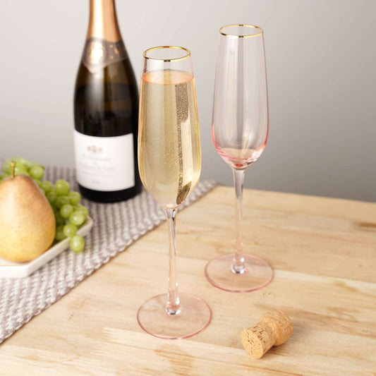 Two champagne flutes with a bottle of champagne on a wooden table.