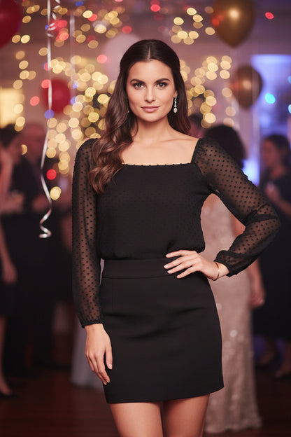 Woman wearing a black top with sheer sleeves and black skirt in a party setting.
