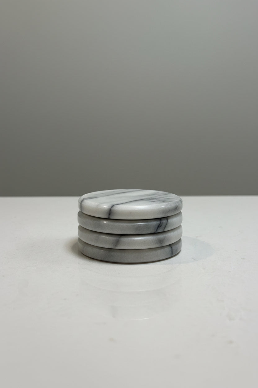 Four round marble coasters with a white and gray veined pattern, arranged in a row on a light gray textured surface.