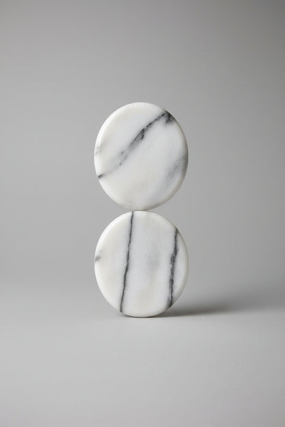 Two smooth polished oval stones with natural gray veining on a blue and green striped textured background.