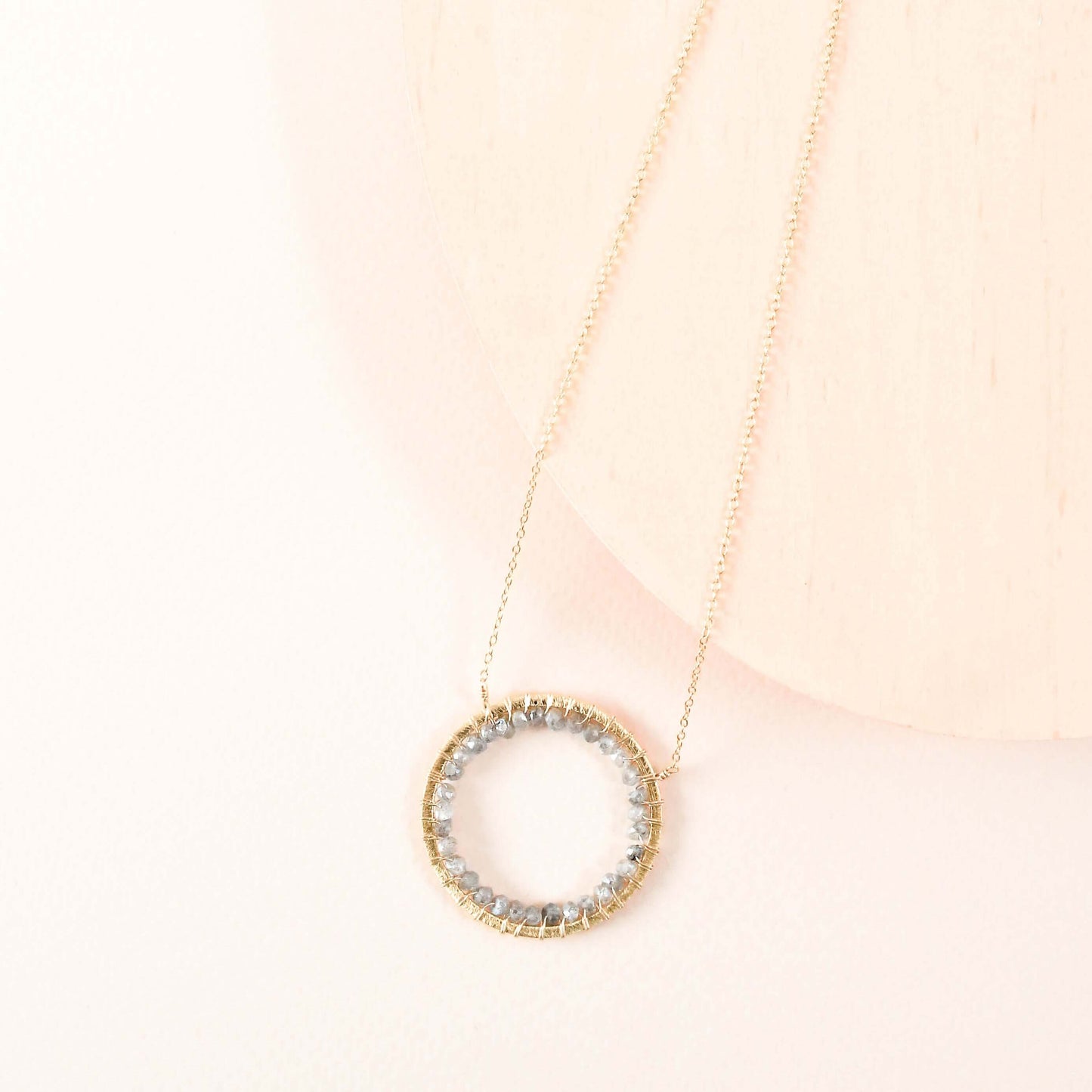 Gold necklace with a circular pendant on a light pink background