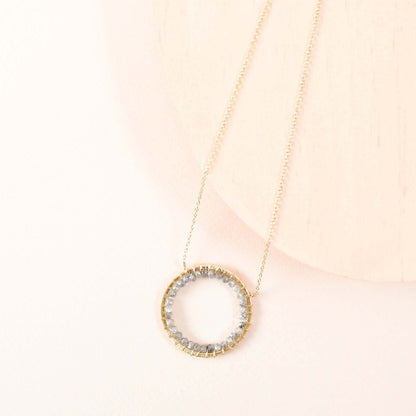 Gold necklace with a circular pendant on a light pink background