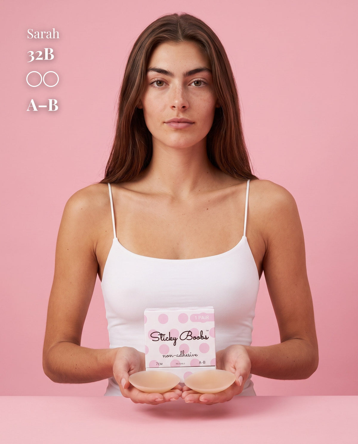Model in a white camisole holding Tan nipple covers and A–B packaging, with a 32B size label.