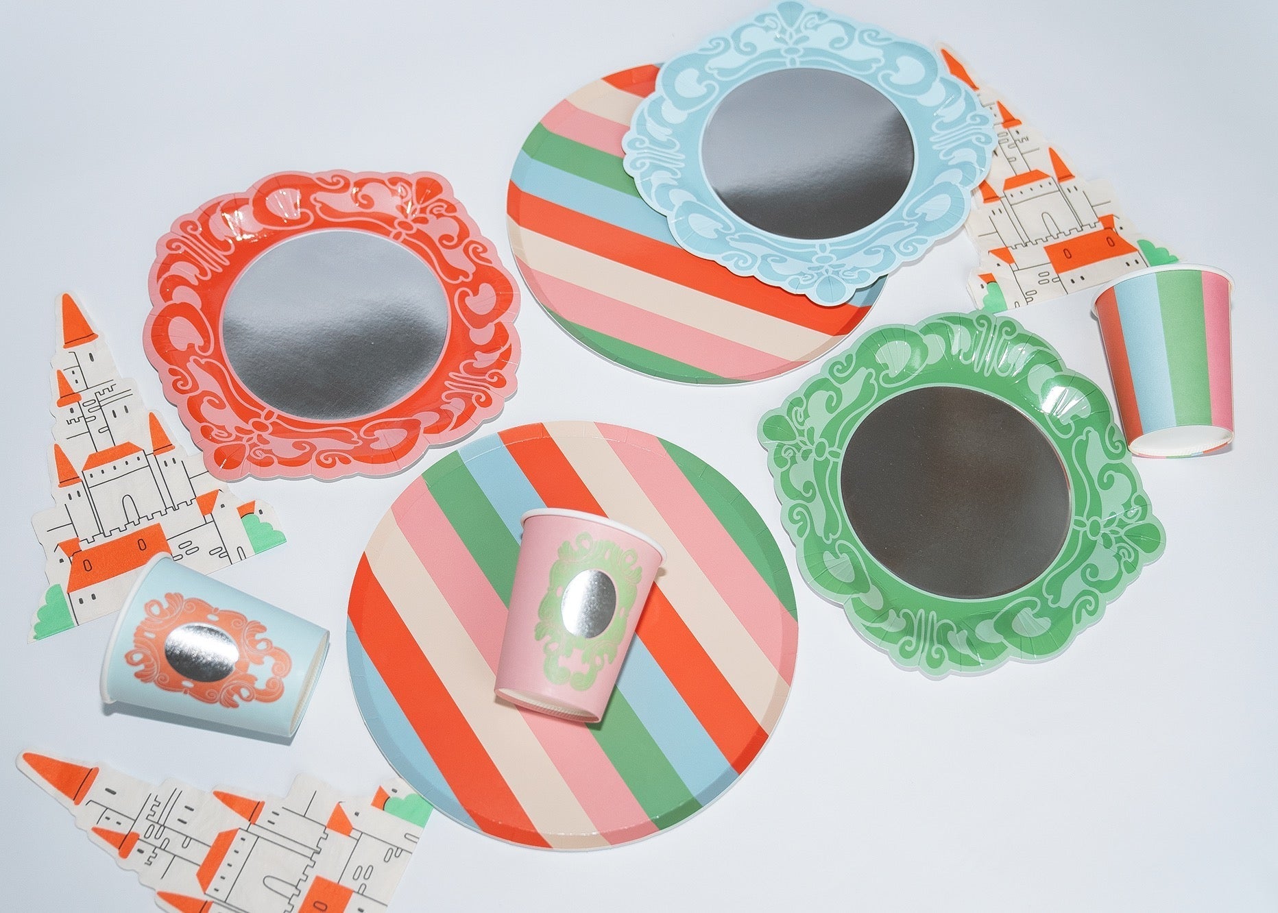 Colorful paper plates, cups, and castle cutouts in pink, blue, and green arranged on a white surface.