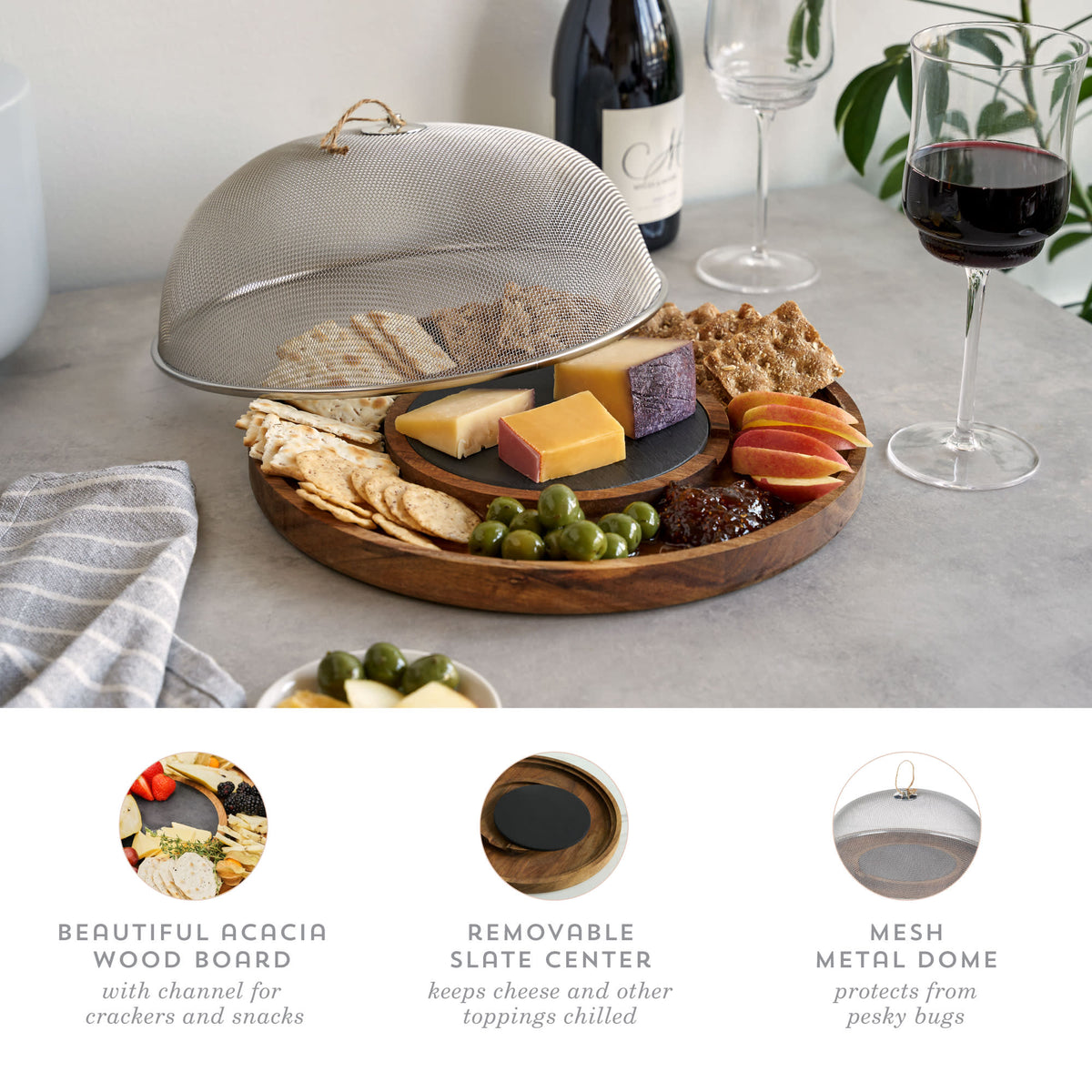 Wooden charcuterie board with cheese, fruits, and meats on a table with wine glasses.