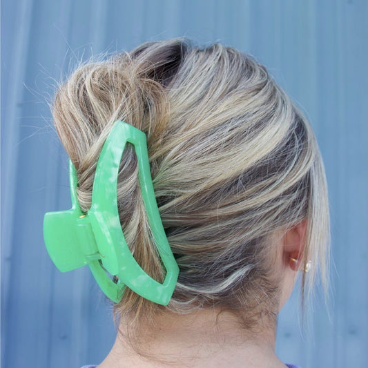 One large green plastic hair clip with an open rectangular frame holding a blonde hair bun in place.