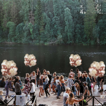 Dandy Decor 60 pack of 12-inch rose gold and white confetti balloons arranged near a lake with people celebrating.
