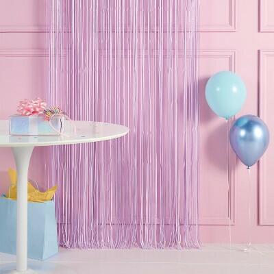 Lavender fringe backdrop with rainbow confetti, paired with a white table and colorful balloons for party decor.