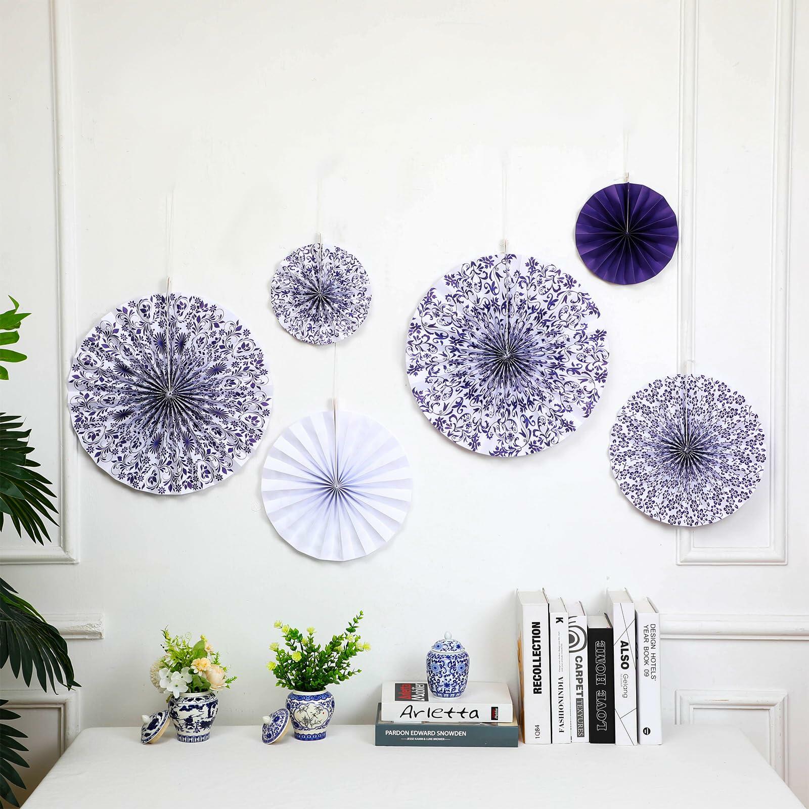 Chinoiserie hanging paper fans in blue and white, featuring floral patterns, arranged on a wall with decorative items below.