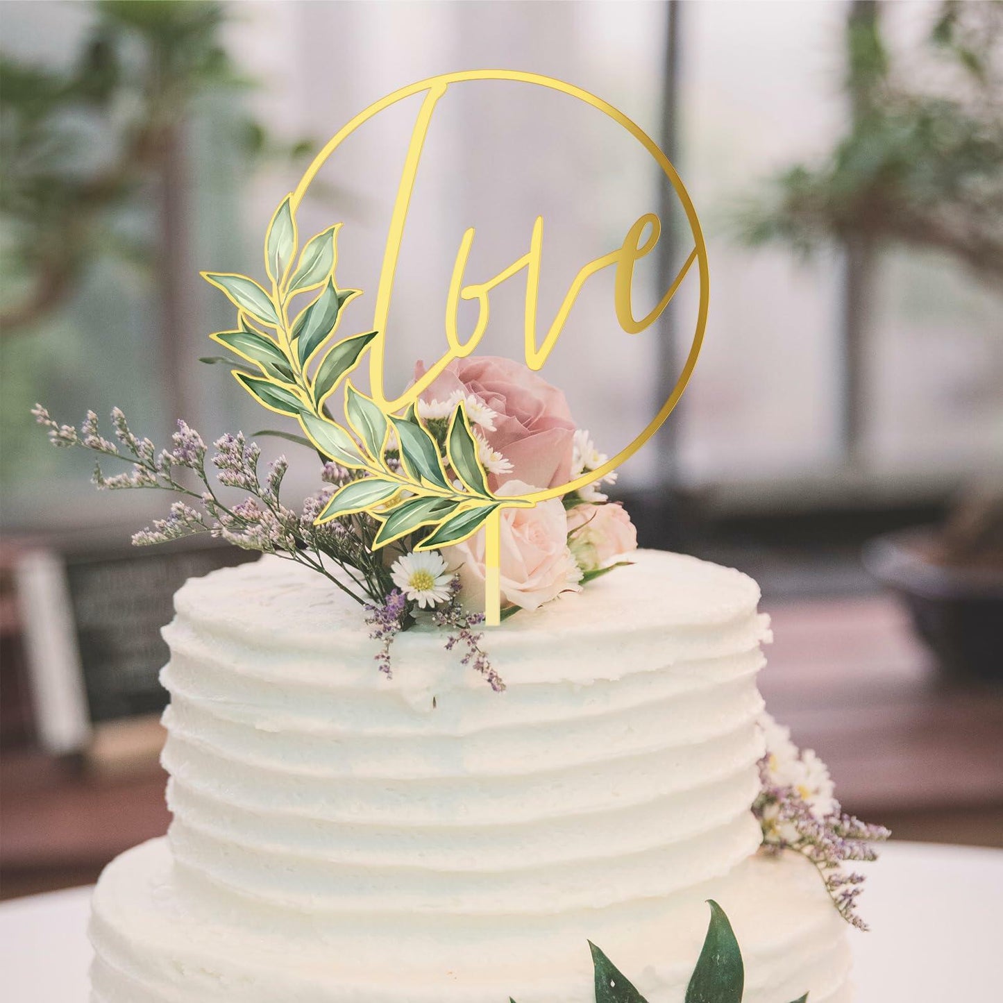 Gold acrylic "love" wedding cake topper with floral accents on a white frosted cake.