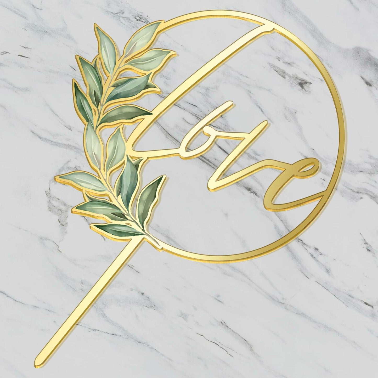 Gold acrylic wedding cake topper featuring the word "love" surrounded by green leaves on a marble background.