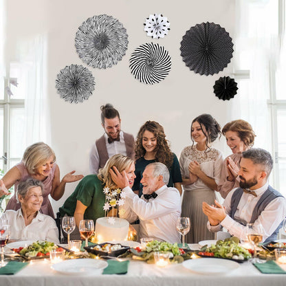 Black hanging paper fans in various designs and sizes, displayed above a celebratory gathering with food and drinks.