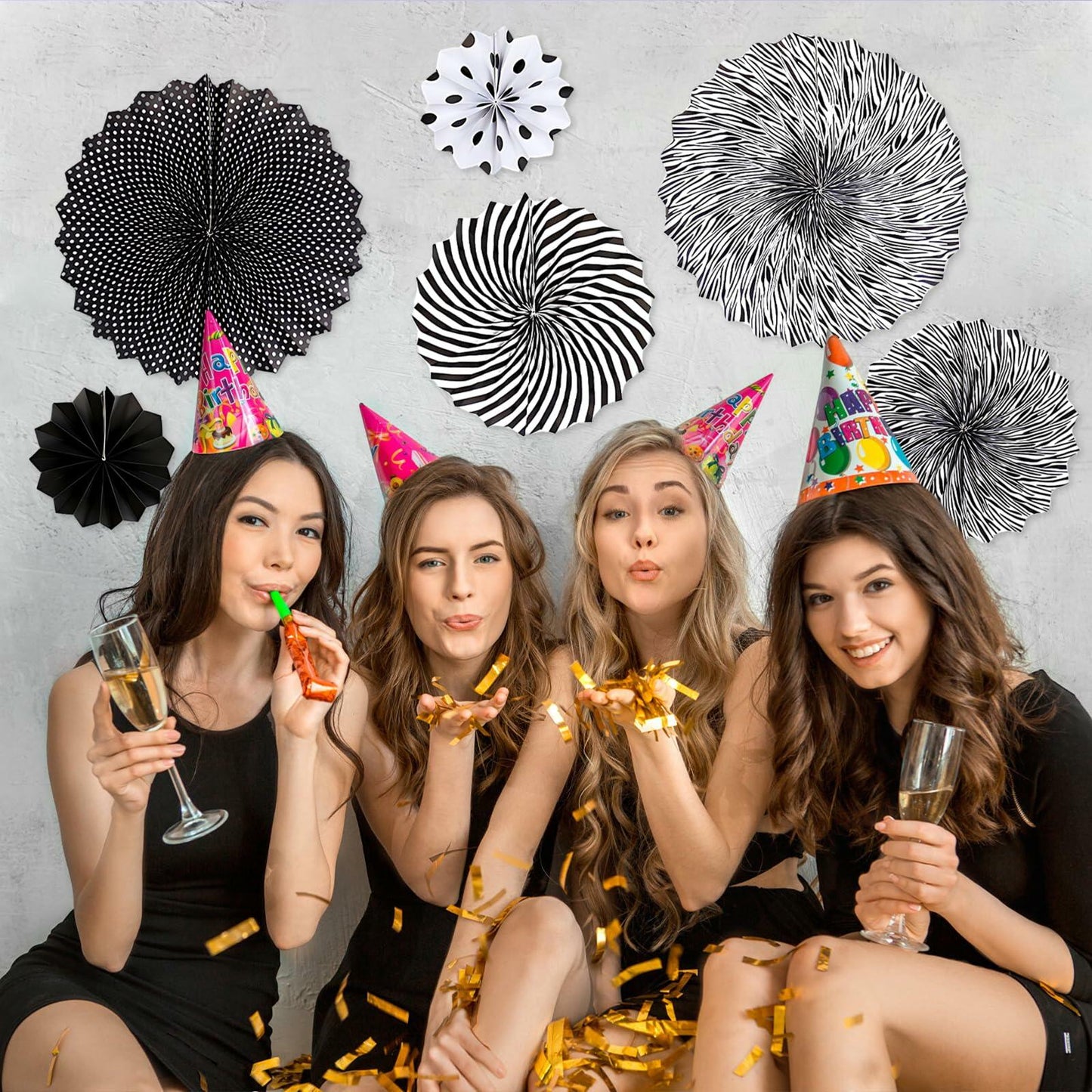 Black hanging paper fans in various patterns, with four women celebrating in party hats, holding drinks and confetti.