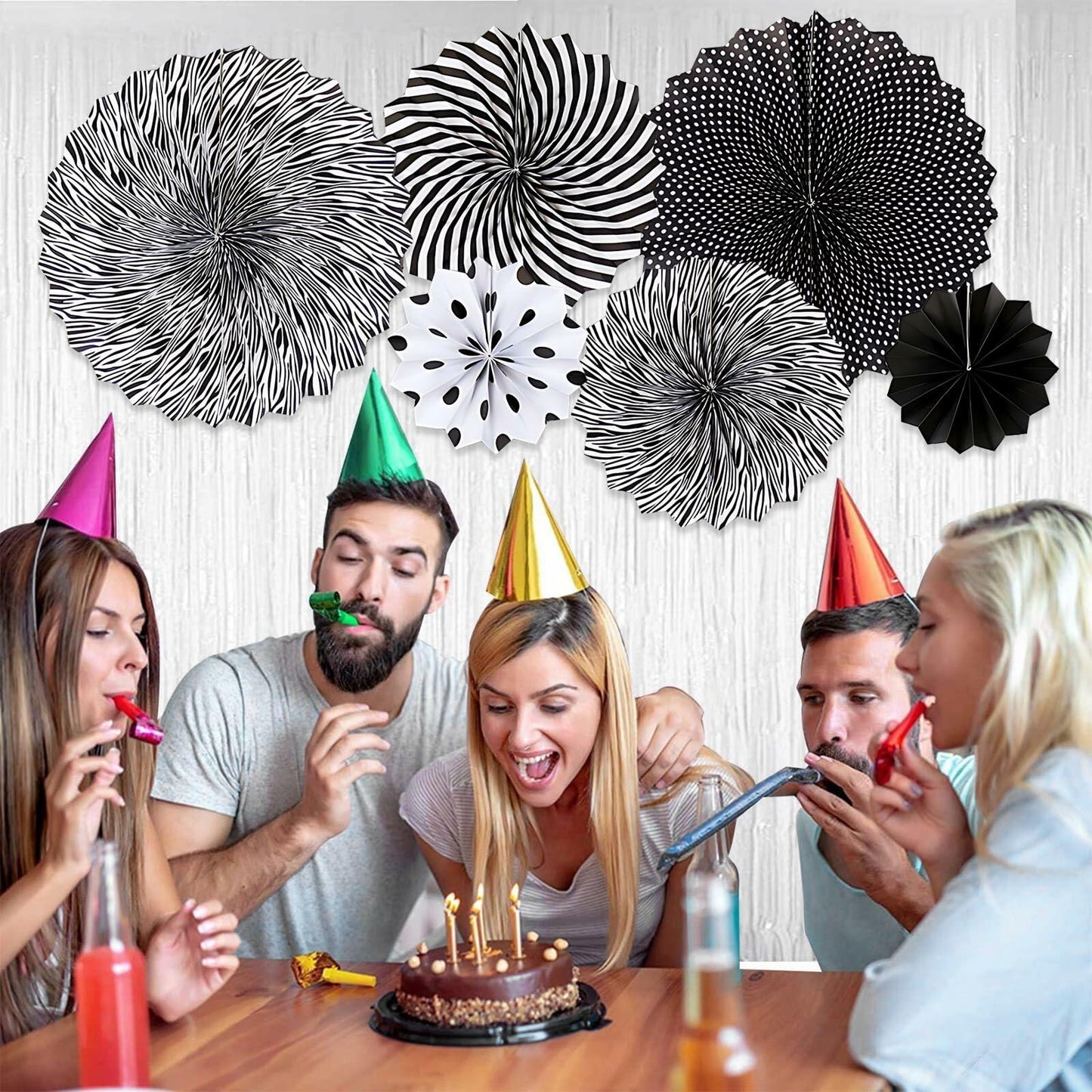 Black hanging paper fans in various patterns and sizes, displayed above a group celebrating a birthday with cake and party...