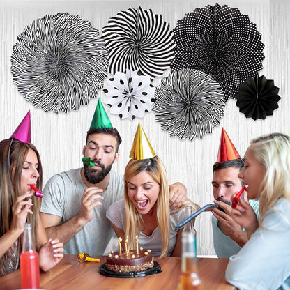 Black hanging paper fans in various patterns and sizes, displayed above a group celebrating a birthday with cake and party...
