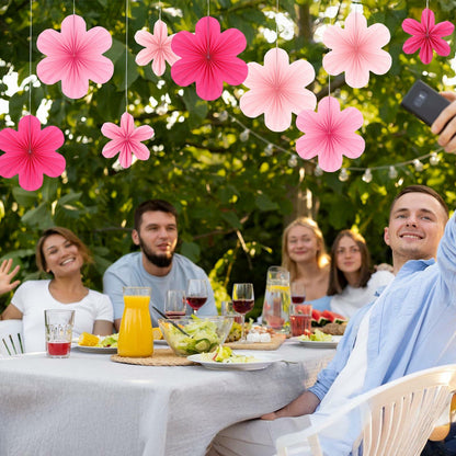 Pink paper fans and flowers hanging above a festive outdoor dining table with people enjoying food and drinks.