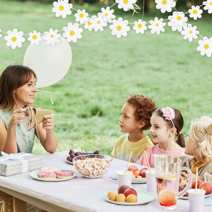 Daisy banner garland in white paper above a picnic table with children enjoying snacks and drinks outdoors.