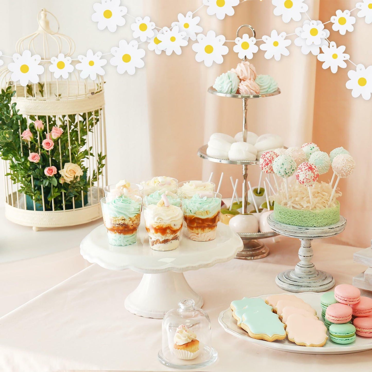 Daisy banner garland above a dessert table with cupcakes, macaroons, and a floral arrangement.