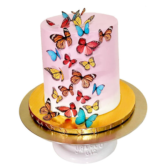 Edible butterflies in mixed colors decorate a pink wedding cake on a gold cake board.