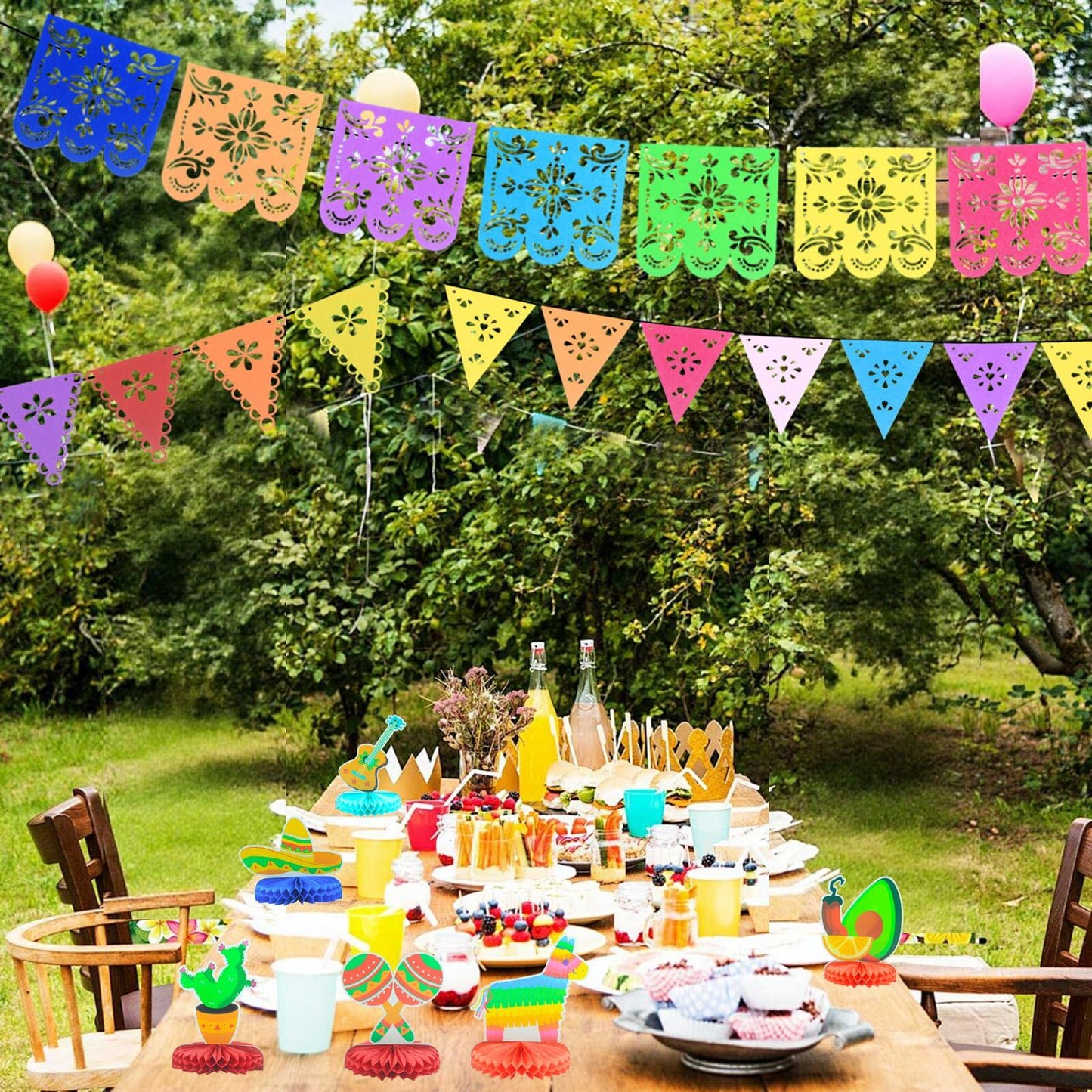 Colorful papel picado banners in various shades hang above a festive table set with party decorations and treats for Cinco...