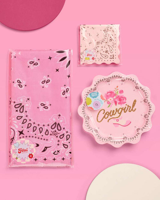 Pink party supplies including napkins, a plate, and a bag on a pink background