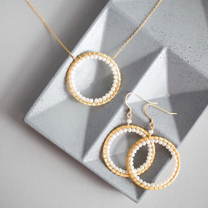 Gold hoop earrings with pearl-like beads on a textured gray surface