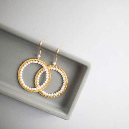 Gold hoop earrings with pearl beads on a gray surface
