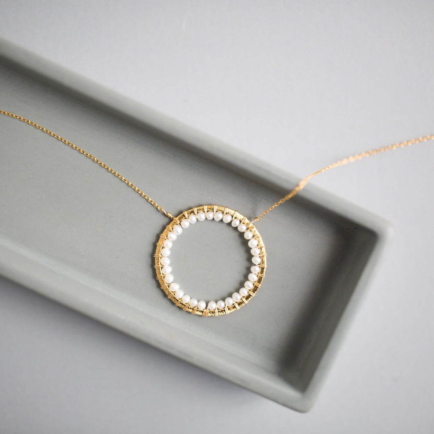 Gold necklace with a circular pendant featuring pearls on a gray surface