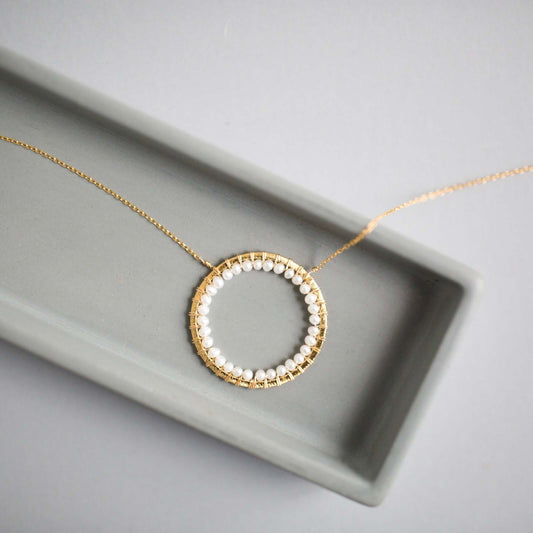 Gold necklace with a circular pendant featuring pearls on a gray surface