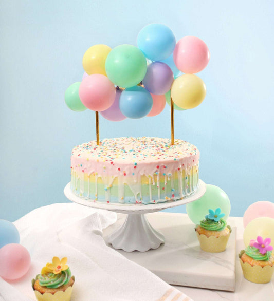 Pastel-colored cake with balloons on a white stand against a light blue background