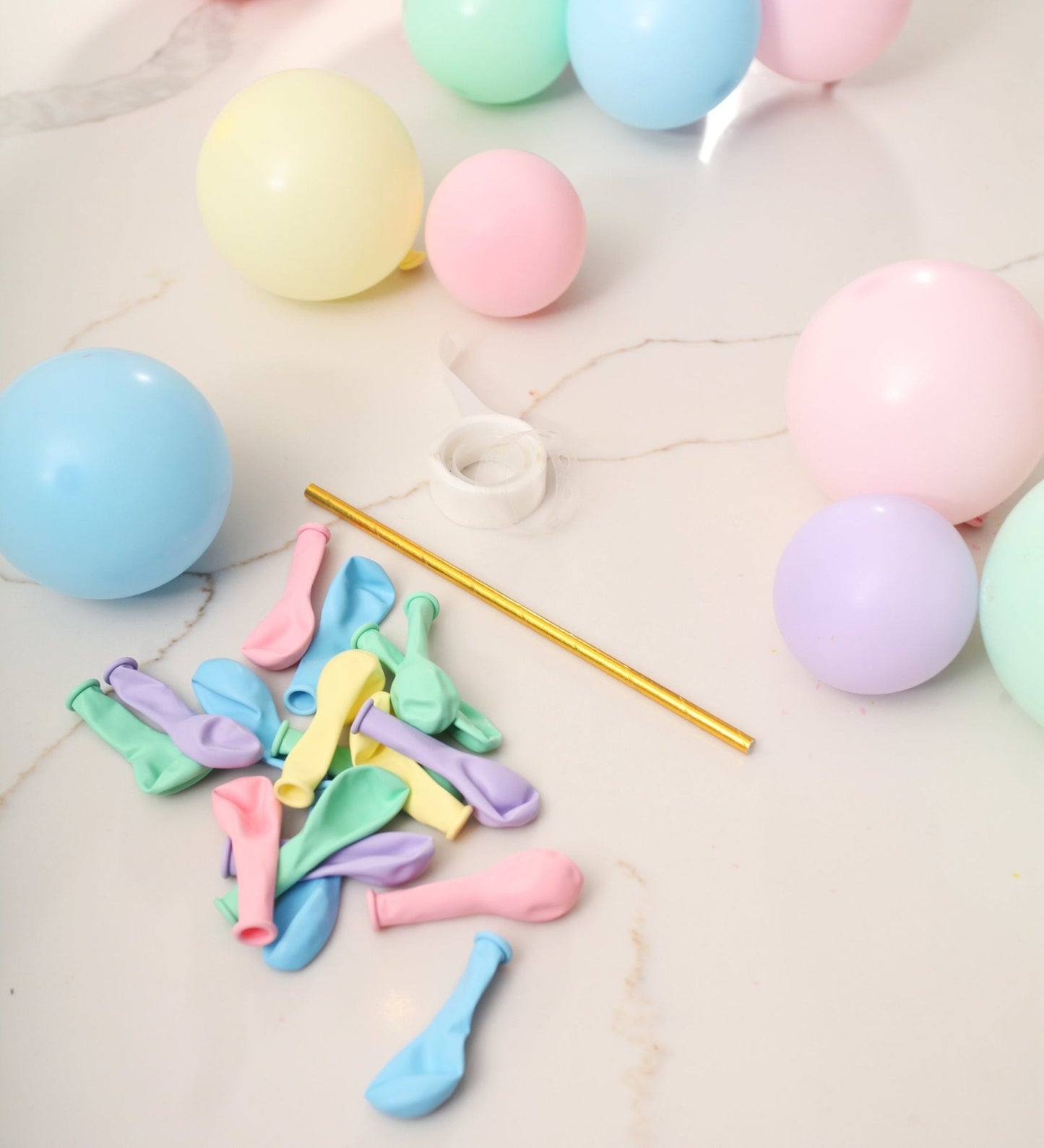 Pastel-colored balloons and a straw on a light surface