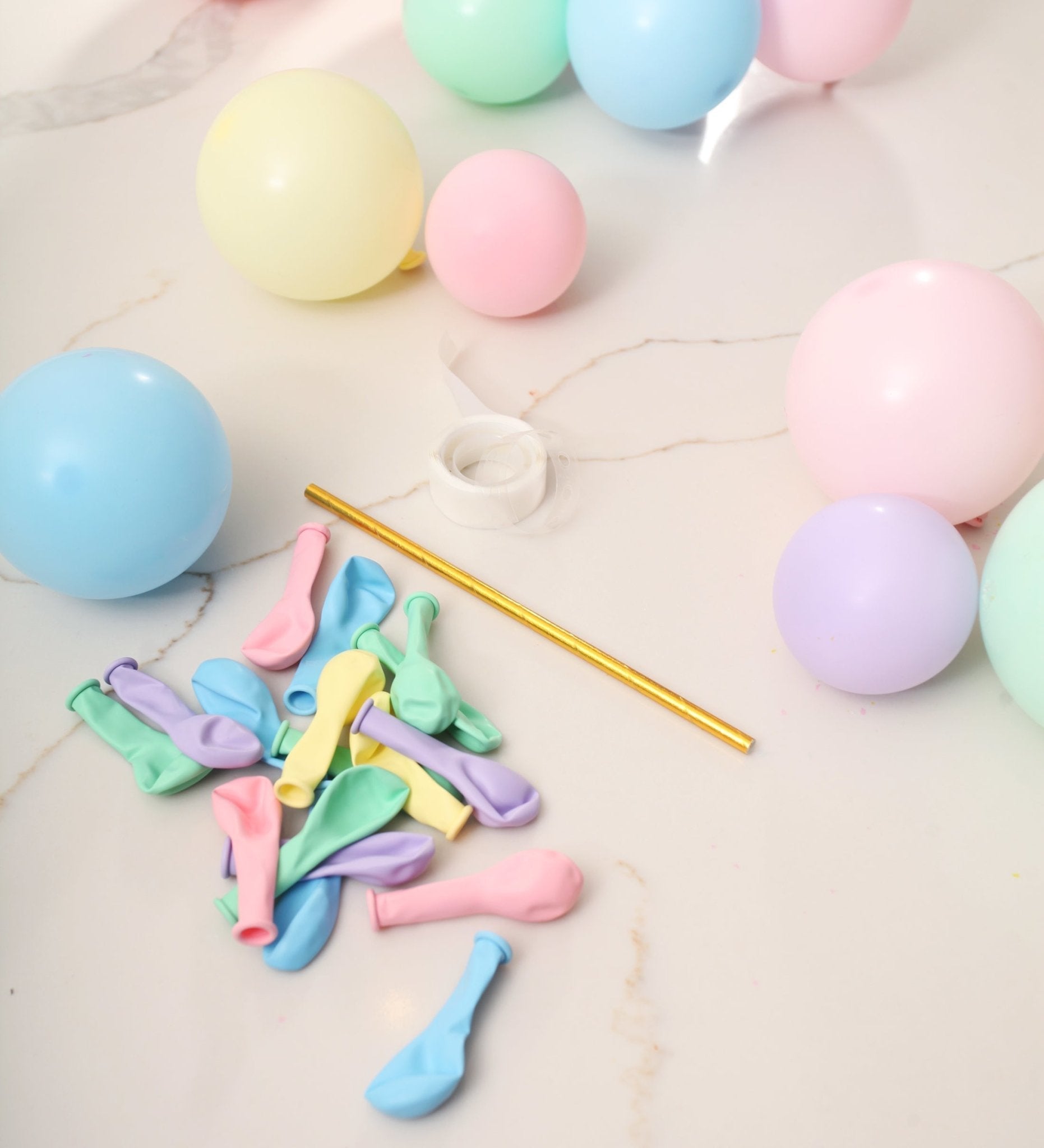 Pastel-colored balloons and a straw on a light surface