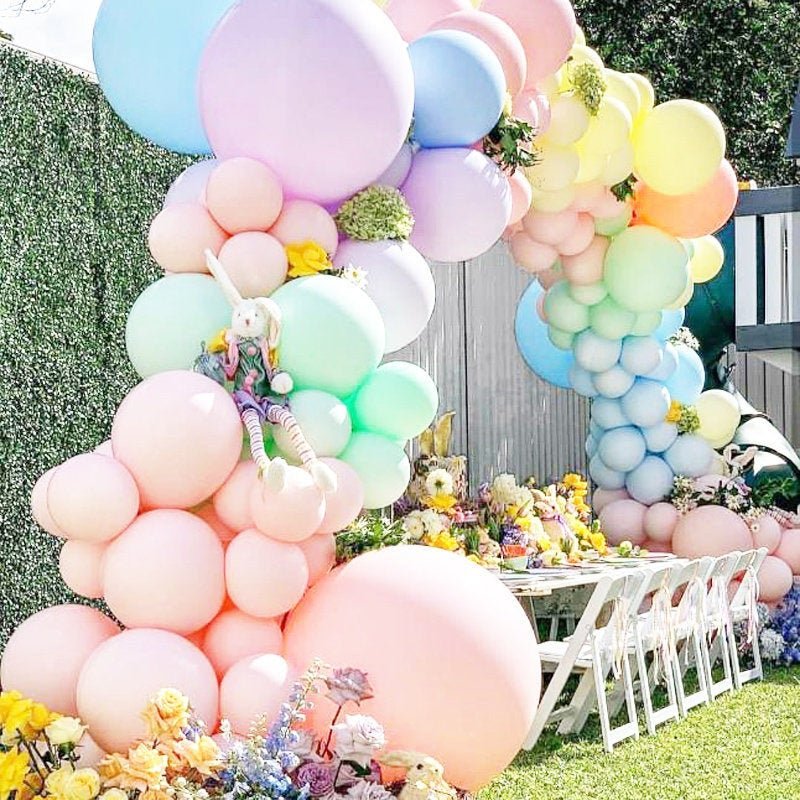 Pastel balloon arch with flowers at a party setup outdoors.