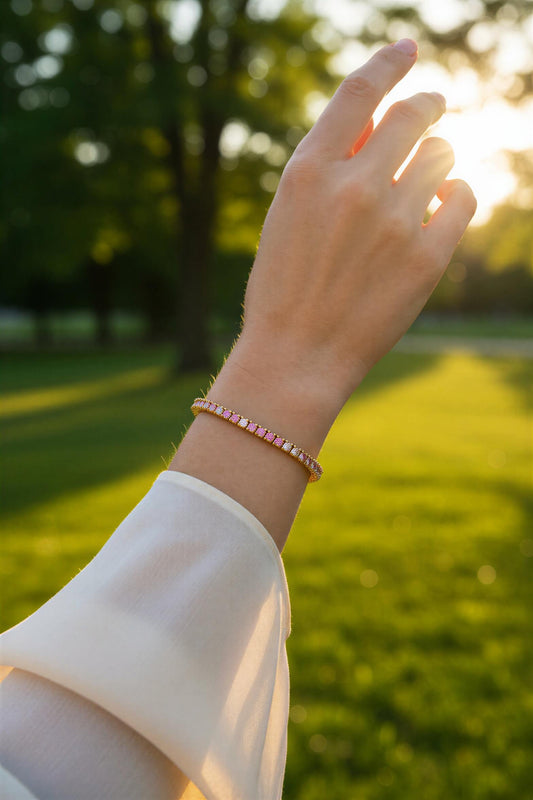 Gold bracelet with pink and white gemstones worn by a person outdoors.