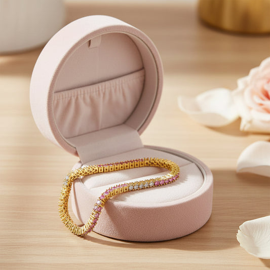Gold bracelet with pink and white gemstones in a velvet box on a wood table.