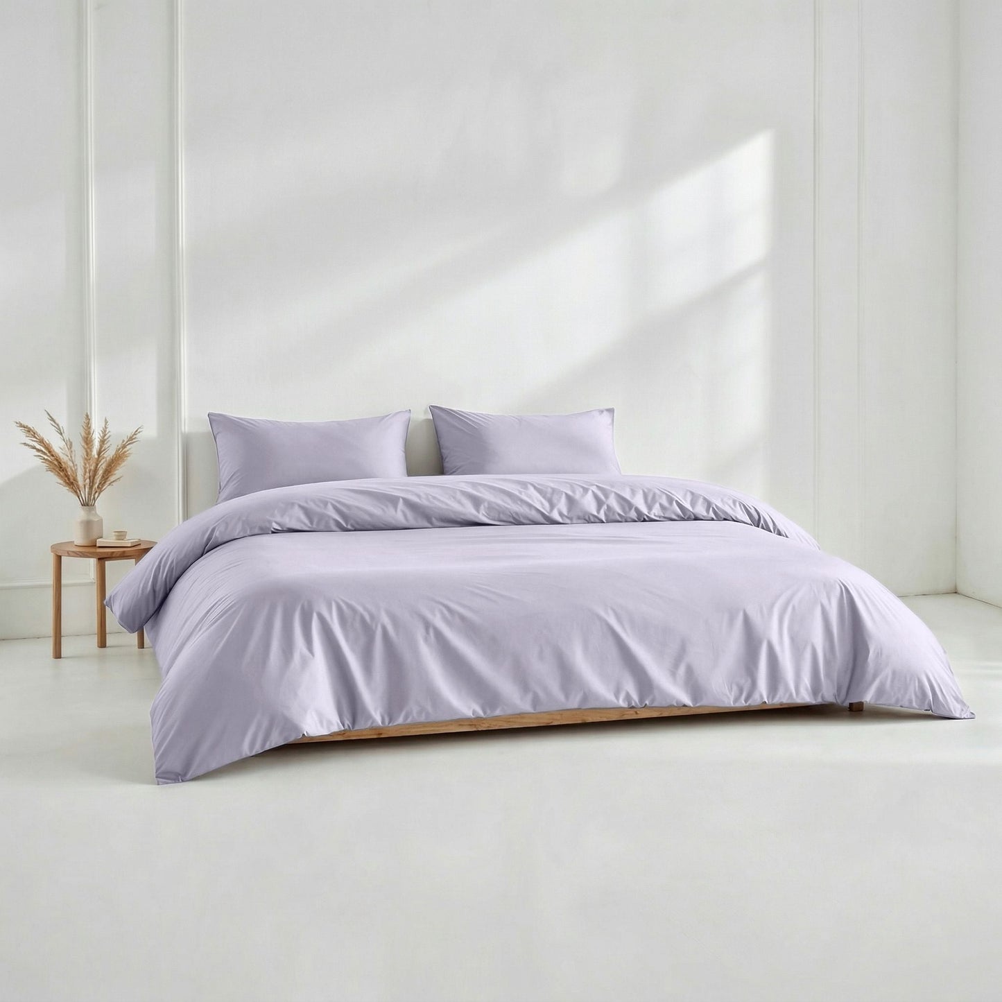 Purple bedding set on a bed in a minimalistic room with a white wall and wooden side table.