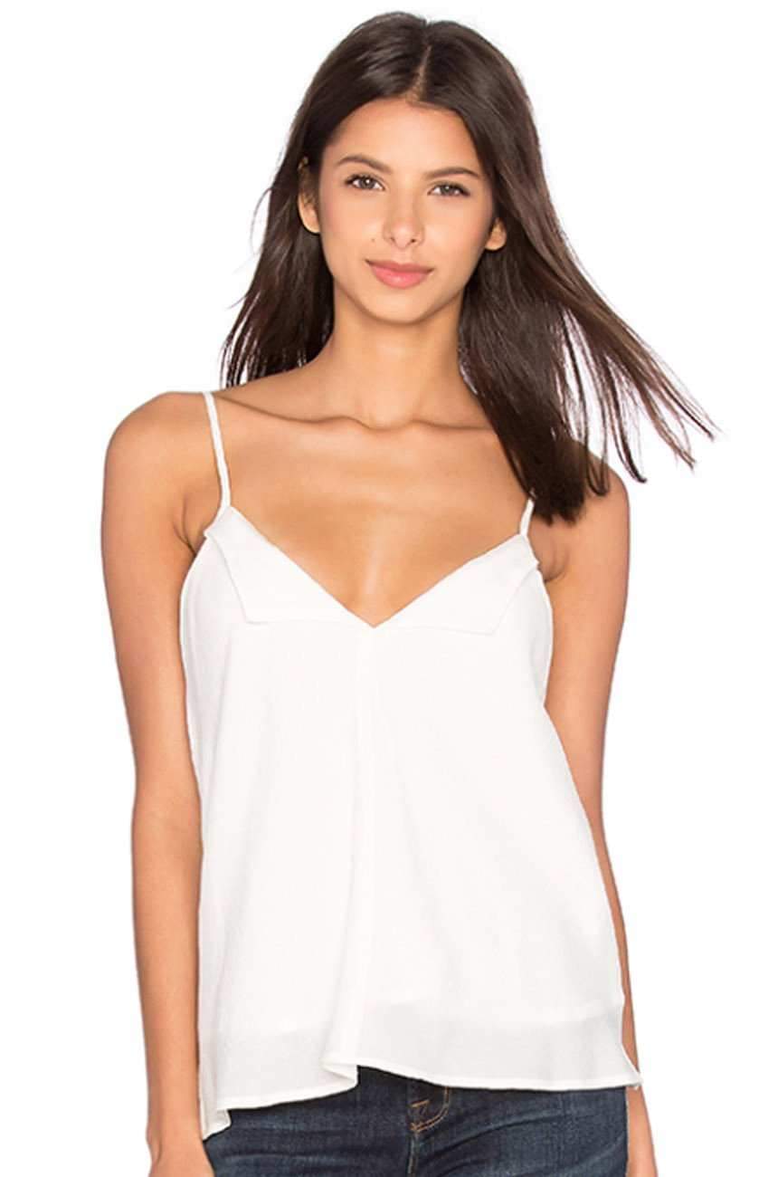 A woman wearing a white spaghetti-strap camisole top and dark blue jeans, photographed against a plain white background.
