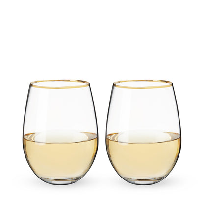 Two stemless wine glasses with gold rims filled with white wine on a white background