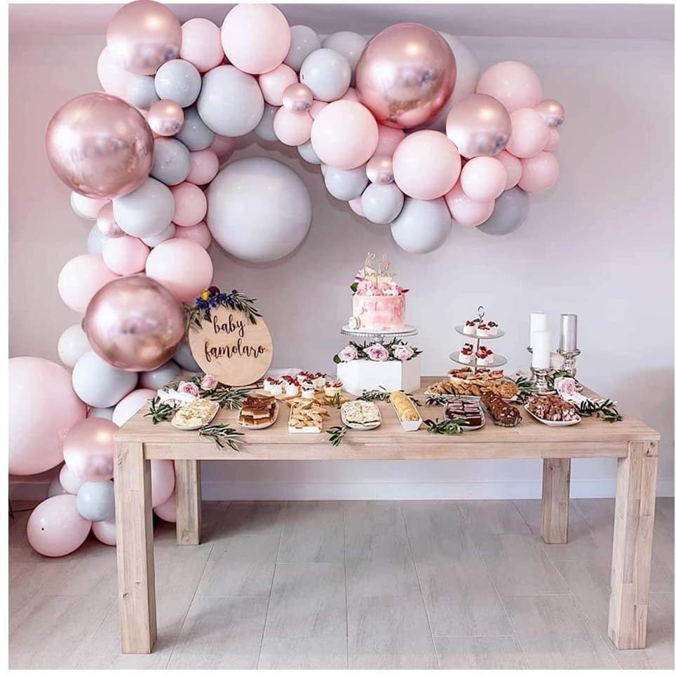 Decorative table with balloons and baby shower decorations against a light pink wall.