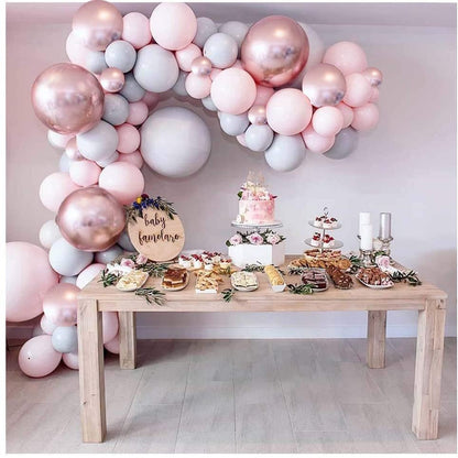 Decorative table with balloons and baby shower decorations against a light pink wall.