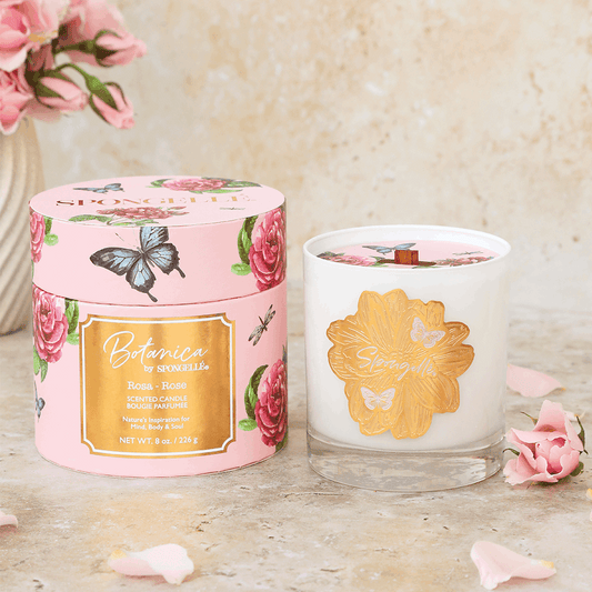 Rose | Botanica candle in a clear glass jar with a gold lid, surrounded by floral packaging and pink rose petals.