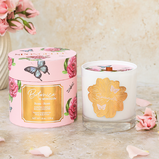 Rose | Botanica candle in a clear glass jar with a gold lid, surrounded by floral packaging and pink rose petals.