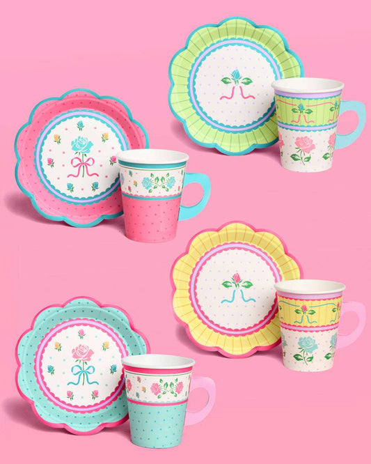 Four floral scalloped paper plates and matching cups in pink, blue, yellow, and green arranged on a pink background.