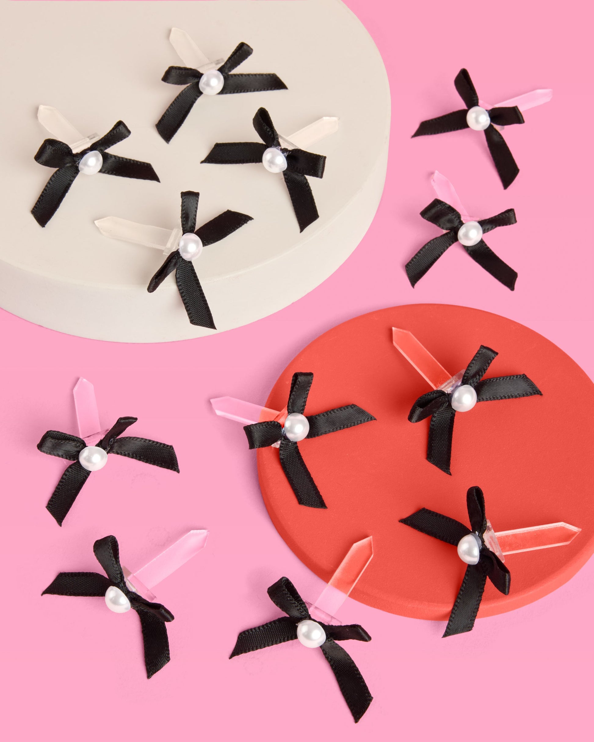 Decorative hair accessories with black ribbons and pearl centers on a pink background