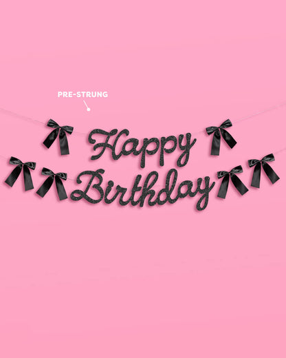 Black 'Happy Birthday' banner with ribbons on a pink background