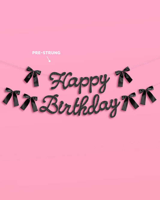Black 'Happy Birthday' banner with ribbons on a pink background