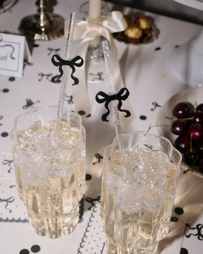 Two glasses with decorative straws on a table with black and white decorations.